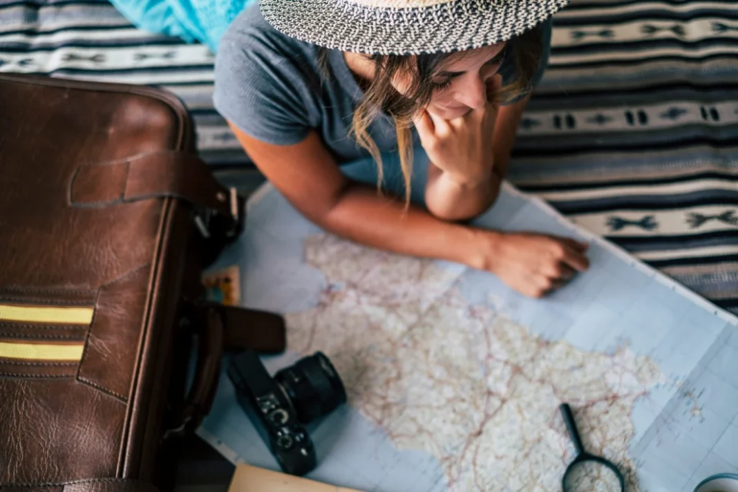 Choose Cheap Flight for Travel” — A traveler studies a map with camera and gear nearby, planning an affordable journey